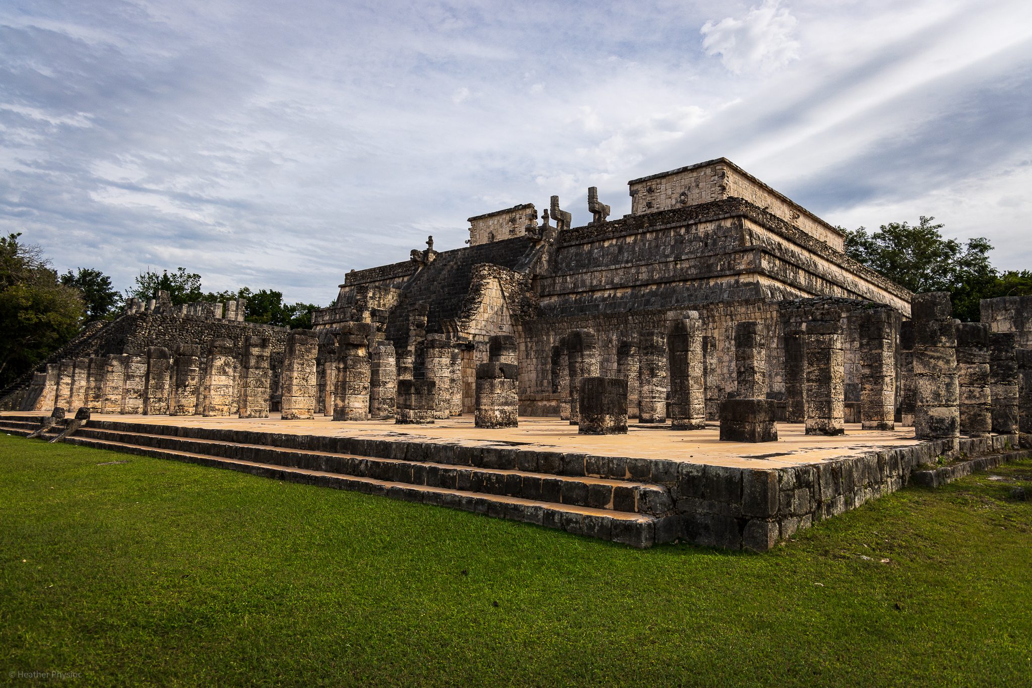 The Temple of the Warriors at Chichen Itza, with its array of stone pillars in the foreground. The intricate carvings on the columns are visible, reflecting the complex Mayan craftsmanship against a dramatic sky.
