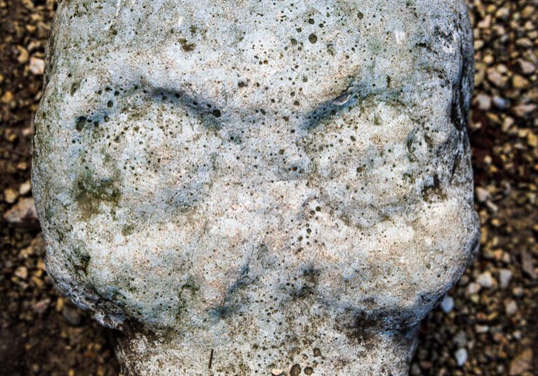 A weathered stone carving of a Mayan skull sits against a pebbled ground, symbolizing the ancient civilization's presence in Coba, Valladolid, within the Yucatan Peninsula of Mexico.